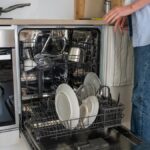 Woman placing dishes and utensils in a dishwasher in a modern kitchen, with light interior. Concept of daily household chores