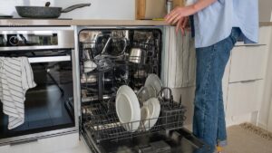 Woman placing dishes and utensils in a dishwasher in a modern kitchen, with light interior. Concept of daily household chores