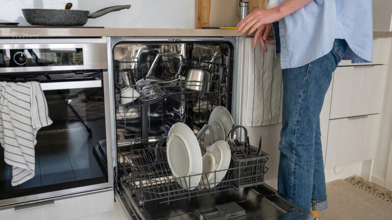Woman placing dishes and utensils in a dishwasher in a modern kitchen, with light interior. Concept of daily household chores