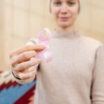 A woman adult with a bald head is holding a pink cancer awareness ribbon, symbolizing support for a cause