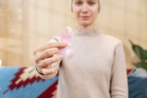 A woman adult with a bald head is holding a pink cancer awareness ribbon, symbolizing support for a cause