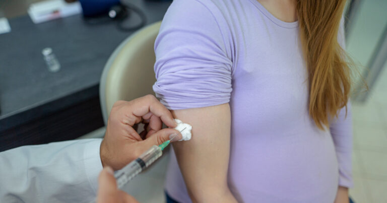 A pregnant young woman receives a vaccine at a preventive examination by a doctor