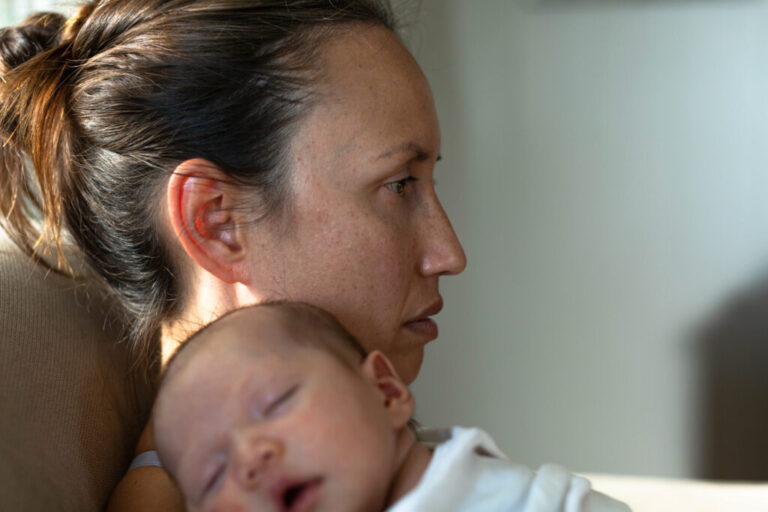 A sad mother sitting at home suffering from postpartum depression. Motherhood problems.