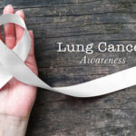 Lung cancer awareness month with white/ light pearl color ribbon on woman's hand support on aged wood